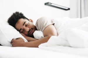 Photo of young african american man with mustache sleeping in white bed